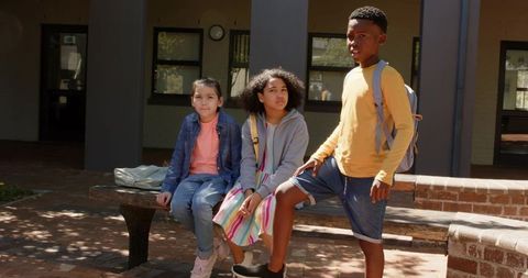 Students sitting and standing on bench in school courtyard with backpacks and casual clothes