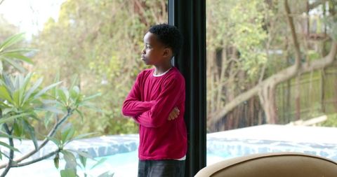 African american boy standing by glass door looking out at backyard pool