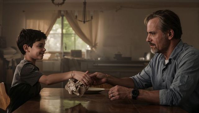 Father and son exchanging crumpled brown parcel at kitchen table, intimate family moment
