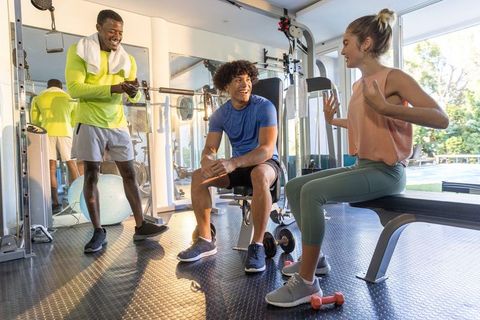 Diverse friends laughing and resting after workout in gym with weights and bench