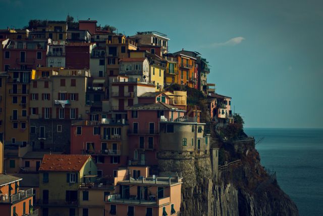 This image showcases the picturesque cliffside village of Manarola in the Italian Riviera at dusk. The vibrant, colorful houses stacked closely together create an enchanting and cohesive architectural scene. Perfect for travel-related materials, Europen destinations promotions, and articles highlighting beautiful coastal towns.