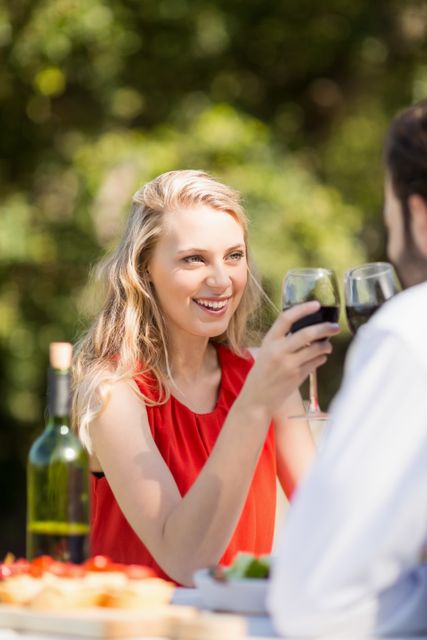 Couple enjoying a romantic meal at an outdoor restaurant, toasting wine glasses and smiling. Ideal for use in advertisements for restaurants, dating services, wine brands, or lifestyle blogs focusing on romance and leisure activities.