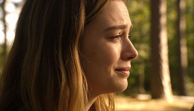 Tearful young woman crying in sunlit forest golden hour portrait conveying grief and solitude