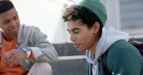 Young african american male students sitting on campus steps, thoughtful friend engaging