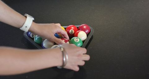 Female hands arranging colorful pool balls in rack on black table with white watch