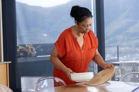 Senior african american woman arranging dining table on balcony with mountain view