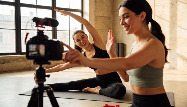 Filming Yoga Tutorial with Two Women Stretching and Smiling in Sunlit Industrial Loft