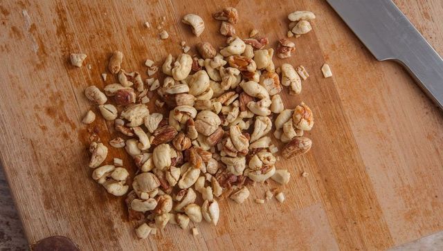 Chopping assorted nuts on rustic wooden cutting board with chef knife, closeup texture