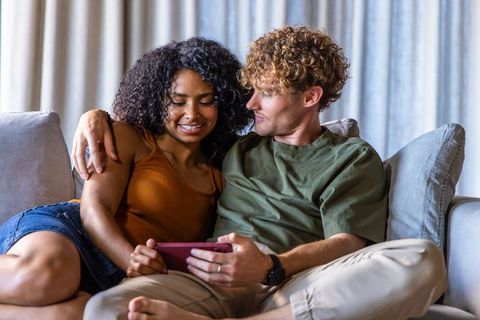 Young couple cuddling on sofa while sharing smartphone, intimate cozy home relaxation