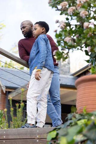 African american father and son standing on deck leaning on railing in quiet reflective moment