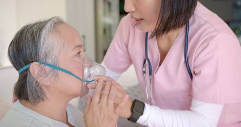 Nurse assists senior woman with oxygen mask at home