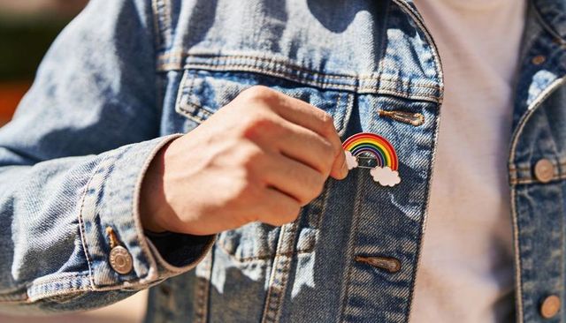 Person pinning rainbow enamel pin on denim jacket closeup colorful fashion detail