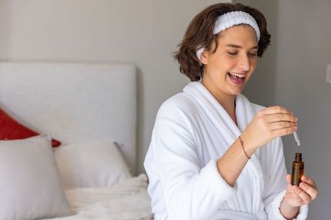 Smiling woman in bathrobe holding amber dropper bottle during morning skincare routine