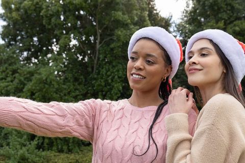 Friends wearing santa hats taking selfie in park amid evergreen holiday cheer