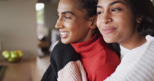 Two young women embracing and smiling being happy in a cozy home environment. Perfect for illustrating themes of friendship, warmth, and happiness in personal blogs, mental health articles, lifestyle magazines, and social media campaigns.