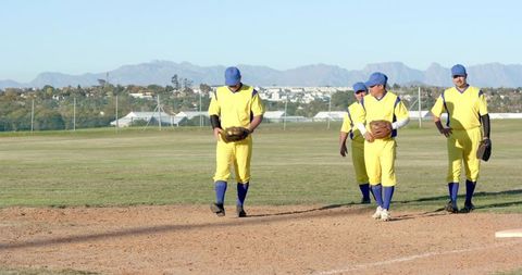 Mature baseball teammates walking on infield holding gloves in yellow-blue uniforms
