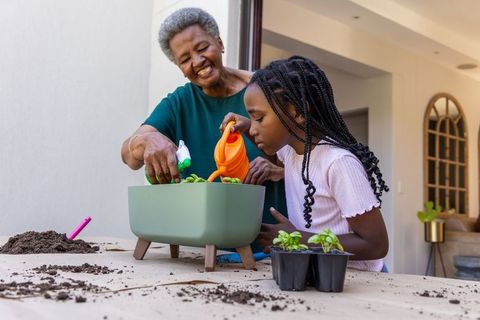Senior african woman guiding youth african girl planting and watering seedlings in planter