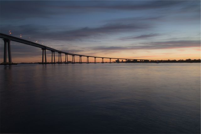 Sunset Over Calm Waters and Long Bridge Silhouette - Download Free Stock Photos Pikwizard.com