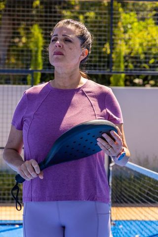 Mature woman holding paddle on sunny outdoor pickleball court wearing purple activewear