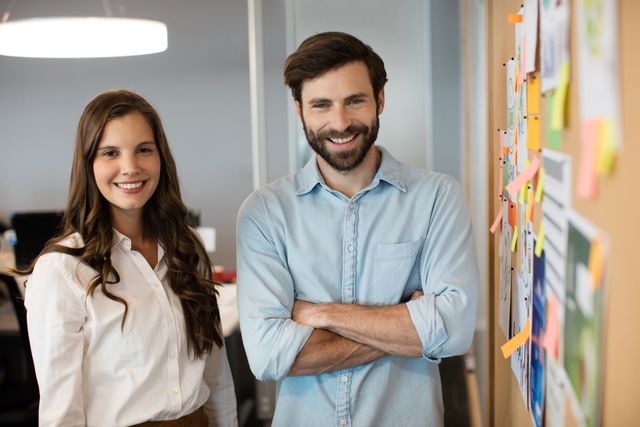 Portrait of smiling business colleagues standing by soft board at office