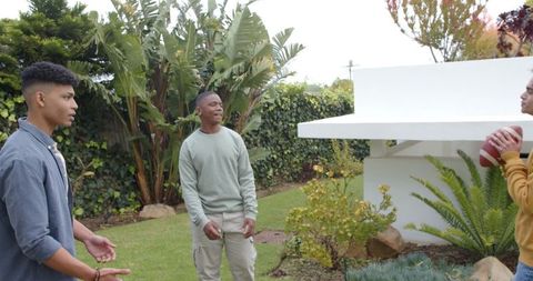 Diverse young men playing catch in backyard laughing and talking with football