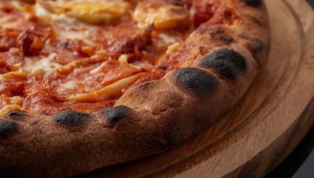 Neapolitan pizza with charred crust resting on wooden board melted cheese and pepperoni