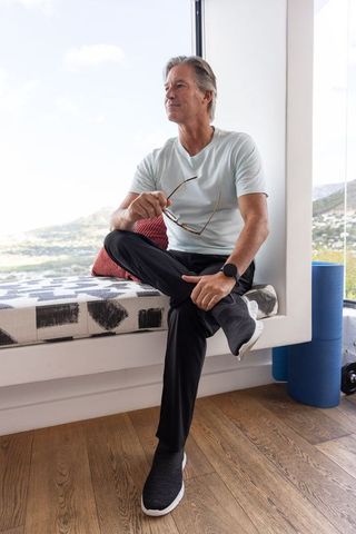 Middle-aged man sitting on window bench holding sunglasses, relaxing with scenic view