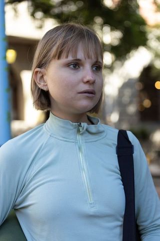 Young woman standing on urban sidewalk wearing mint zip-up, shoulder bag, nose ring