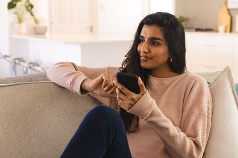 Relaxed woman checking smartphone at home in cozy living room