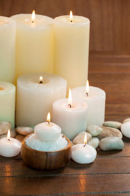 Candles with massage oil bottles and sea salt in wooden bowl on table
