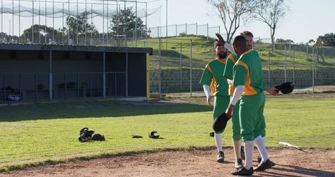 Baseball teammates exchanging high five on infield near dugout in green yellow uniforms