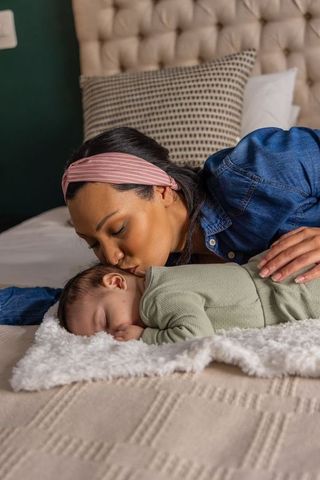 Mother kissing sleeping newborn on cozy bed, tender maternal bonding and affection