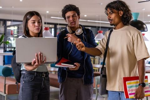 Multicultural college students collaborating around laptop in modern campus study lounge