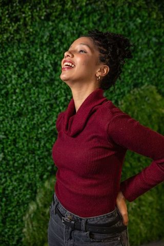 Joyful african american woman laughing in maroon sweater against lush green hedge