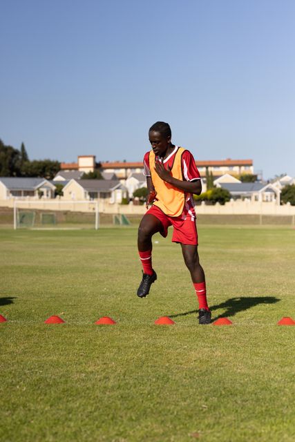 African american dedicated player in jersey and sports bib exercising over cones against clear sky. Copy space, playground, summer, unaltered, sport, competition, exercising, training and fitness.