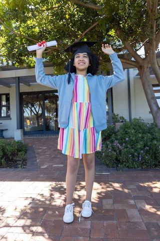 African american girl wearing mortarboard with diploma celebrating graduation outdoors
