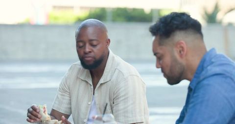 Two diverse friends enjoying casual outdoor lunch with wrap and drinks in urban scene