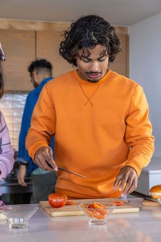 Multicultural friends preparing fresh tomatoes in modern kitchen while man slices