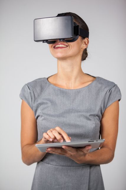 Woman holding digital tablet and using virtual reality headset against white background