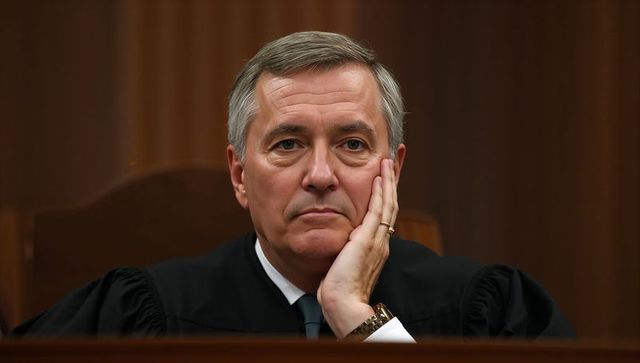 Contemplating senior judge resting cheek on hand wearing robe and wedding ring