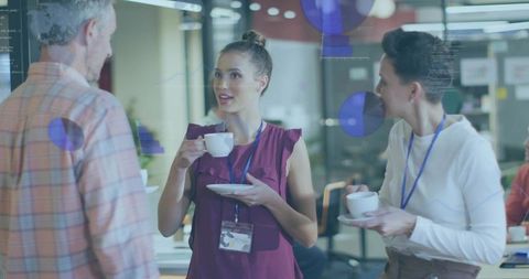 Coworkers chatting over coffee in modern open office with glass partition and lanyards