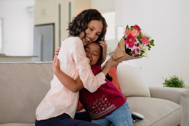 Happy hispanic mother holding flowers and hugging daughter on sofa. family spending time together at home.