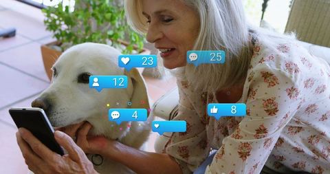 Senior woman enjoying smartphone with white dog and social notification bubbles on patio