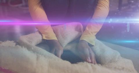 African american woman sifting dark grains from burlap sack on lap with purple lens flare