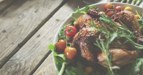 Rustic roasted chicken with rosemary and cherry tomatoes on bed of greens