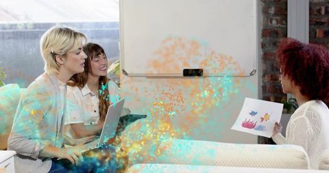 Collaborating women reviewing fish sketch with laptop and whiteboard in coworking lounge