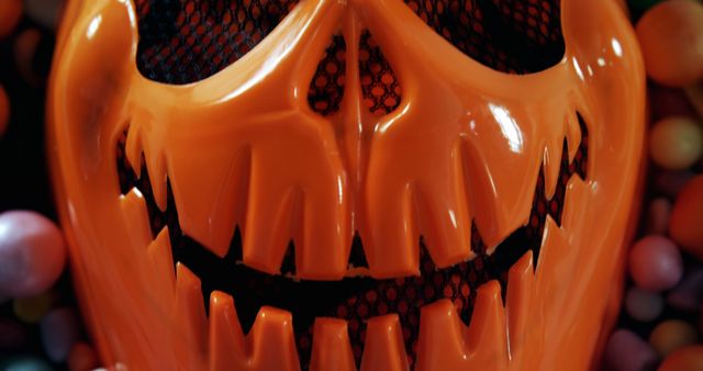 Close-up of an orange pumpkin head mask with intricate carvings suitable for use in Halloween-themed content. Perfect for promoting horror-themed parties, seasonal decorations, or costume ideas. Ideal for creating festive, spooky atmosphere in advertisements, social media posts, and blogs.