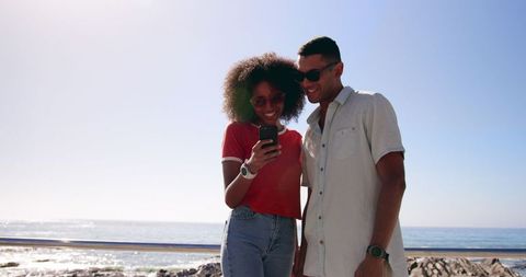 Smiling Couple Enjoying Day Using Smartphone on Beach Walk