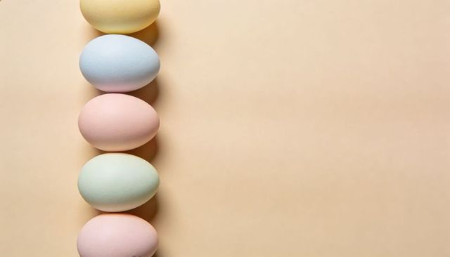 Vertical line of five pastel easter eggs lining left side on beige background with copy space