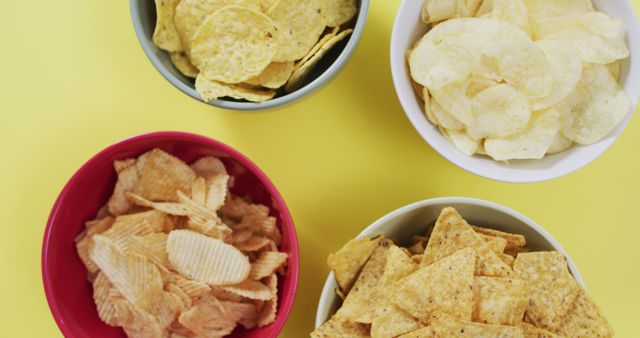 Close up of four bowls full of variety of chips with copy space on yellow surface. food and snack concept